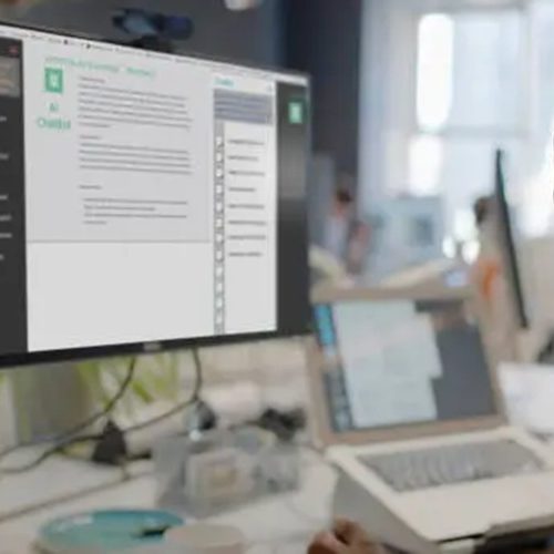Stock image showing a black man?s face looking into a computer screen in an open plan working office. Type is being added to the screen by an Artificial intelligence,  AI,  chatbot.